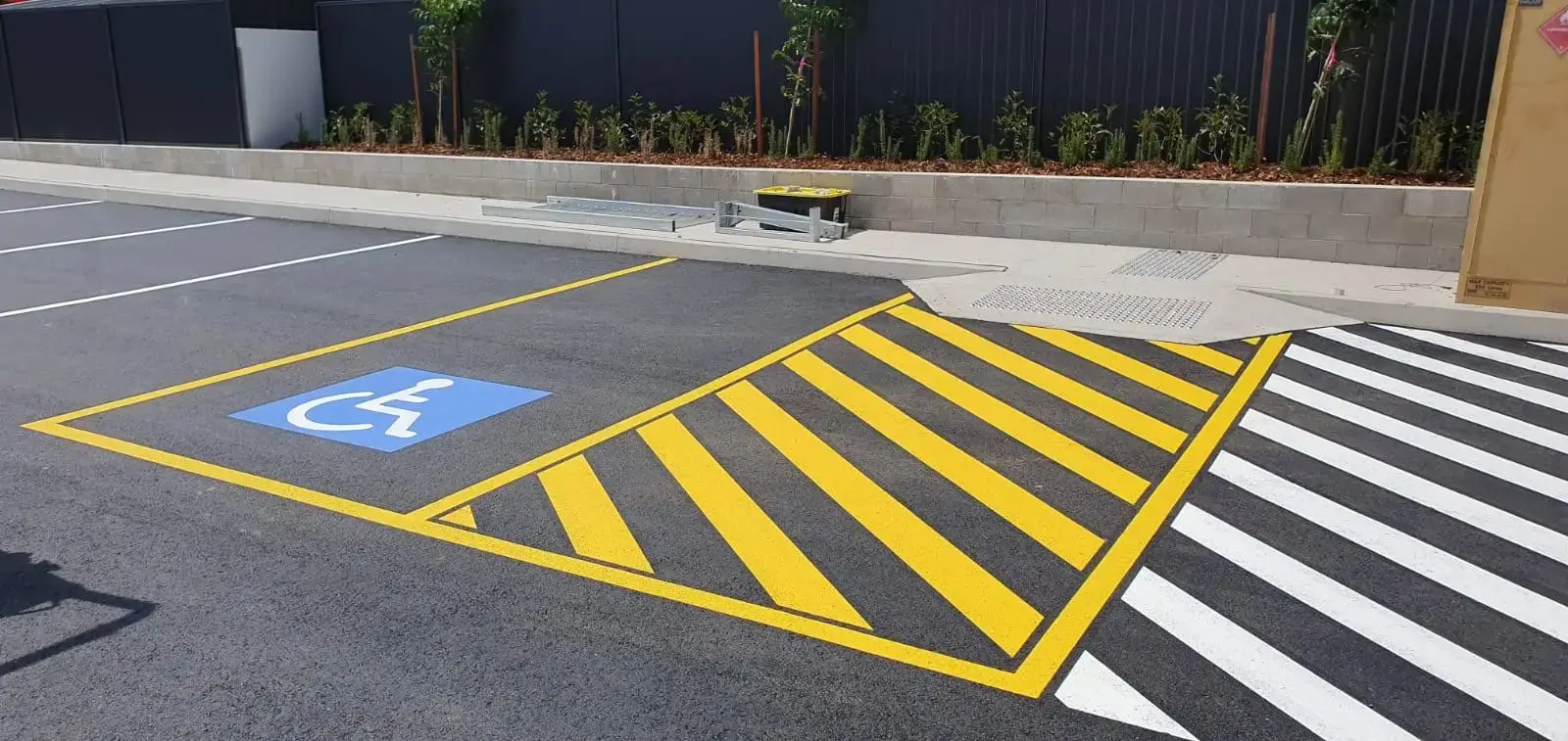 AS 2890 compliant disabled parking bay with blue wheelchair symbol, yellow safety chevrons and white pedestrian crossing