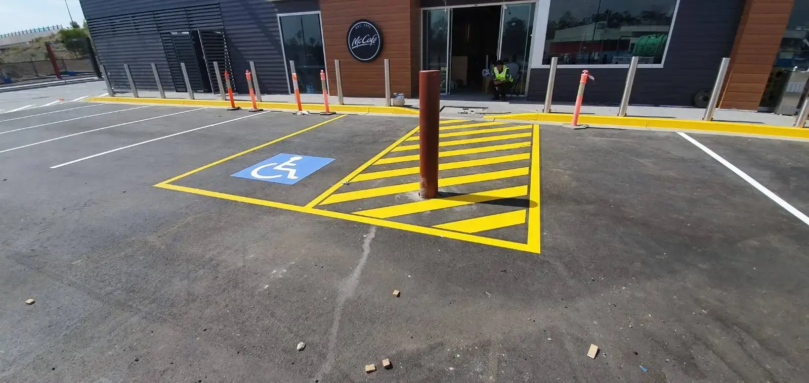 Disabled parking bay with blue wheelchair symbol, yellow chevron safety markings and bollard protection at a Brisbane fast food restaurant