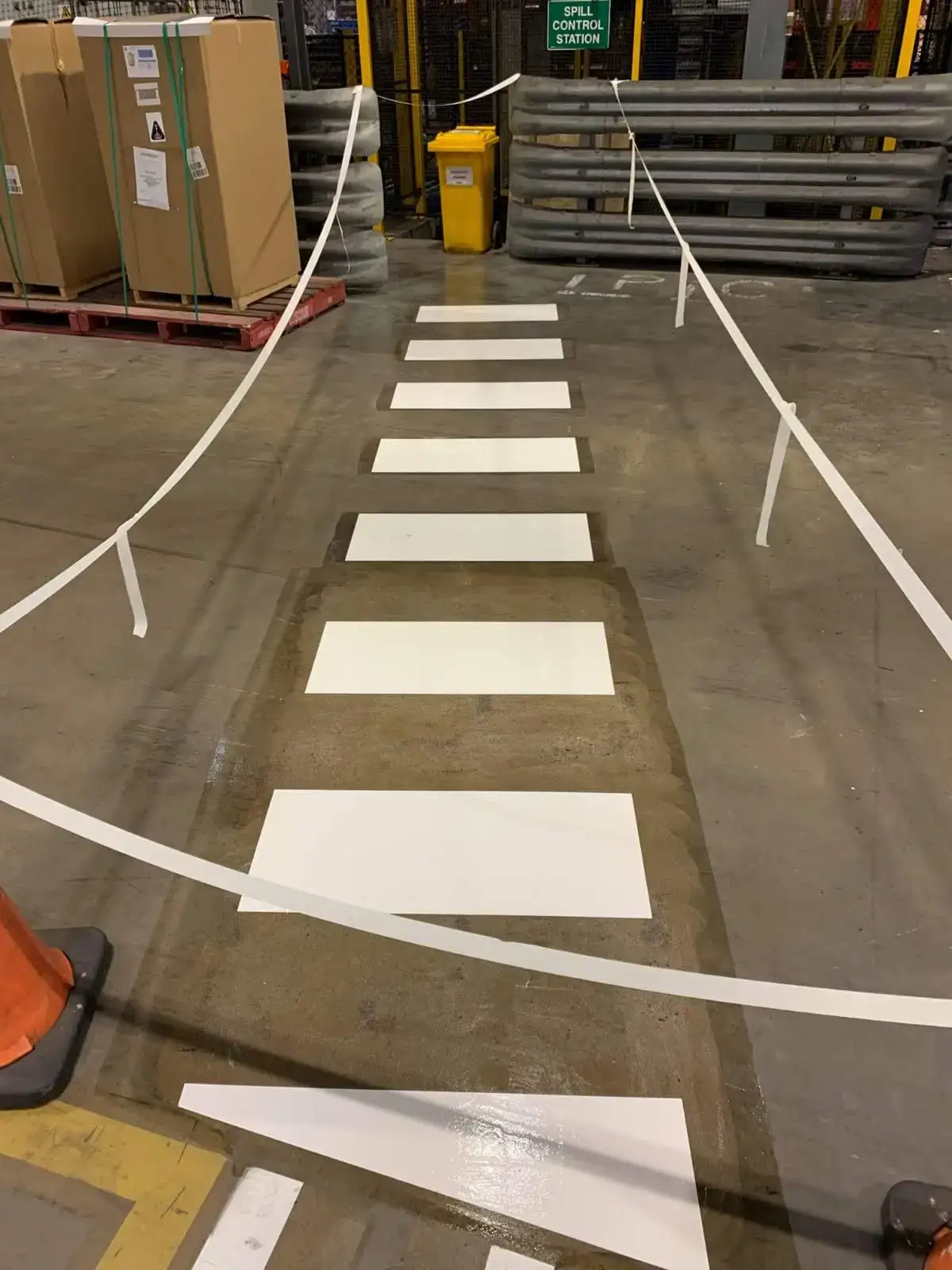 White pedestrian crossing bars with safety barriers and forklift lanes inside a warehouse
