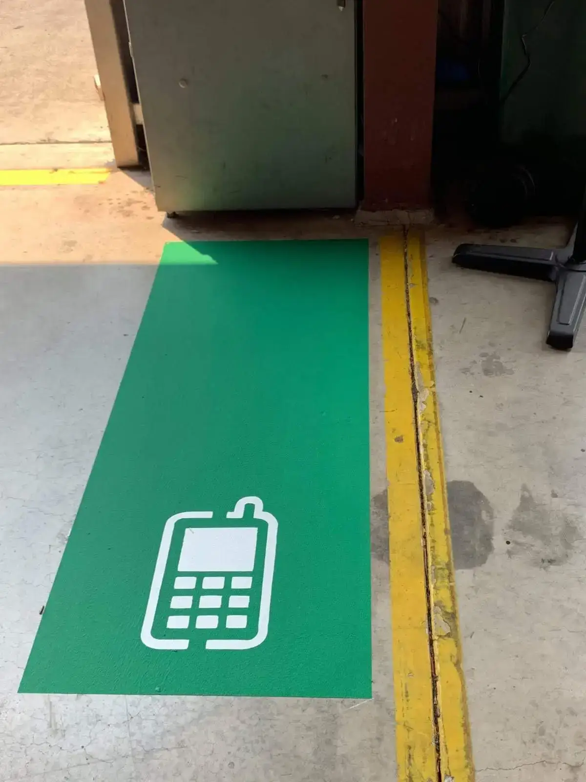 Green mobile phone zone with white icon painted on a warehouse floor